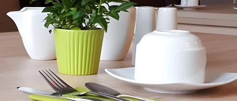 A dining table with a green vase of red flowers, white plates, and cutlery.