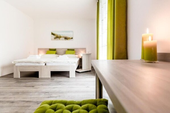 Un dormitorio moderno con una cama de madera, cojines verdes, una mesita de noche con una vela y un cuadro en la pared.