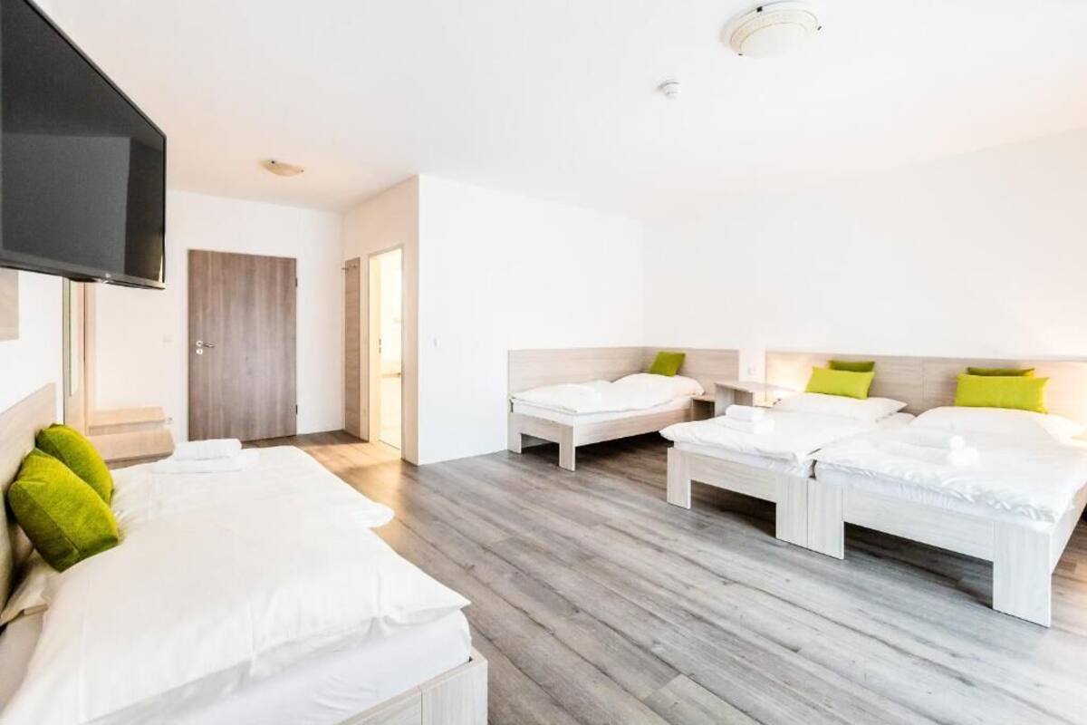 A hotel room with two single beds and a double bed, all with white bedding and green pillows.