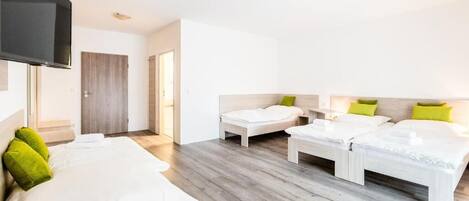 A hotel room with two single beds and a double bed, all with white bedding and green pillows.