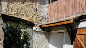 Ein schmaler Innenhof mit einem kleinen Baum, einer weißen Tür und einem hölzernen Balkon.