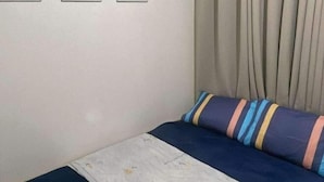 Une chambre à coucher avec un lit, un oreiller, un rideau et un interrupteur fixé au mur.