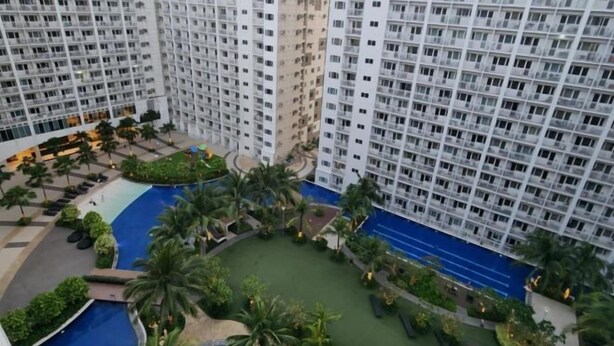 Un immeuble résidentiel de grande hauteur doté de nombreux balcons, d’une cour intérieure agrémentée de palmiers et d’une piscine.