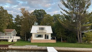 Una casa con balcón que da a una extensión de agua, rodeada de árboles y césped.