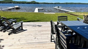 Una terraza de madera con asientos al aire libre, un muelle que se adentra en un lago y un área con césped.
