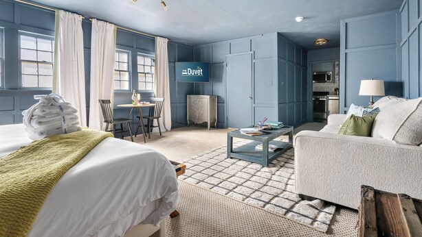 Une chambre d’hôtel comprenant un lit, un canapé, une table à manger avec des chaises, une table basse et une pancarte indiquant « Couette ».