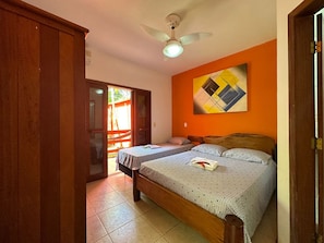 A bedroom with a bed, a ceiling fan, a door, and a wall with a geometric painting. - Pousada Sunset (Itacaré)