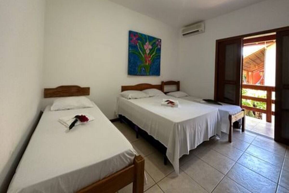 Una habitación con tres camas individuales, un cuadro en la pared y una puerta abierta que da a un balcón.