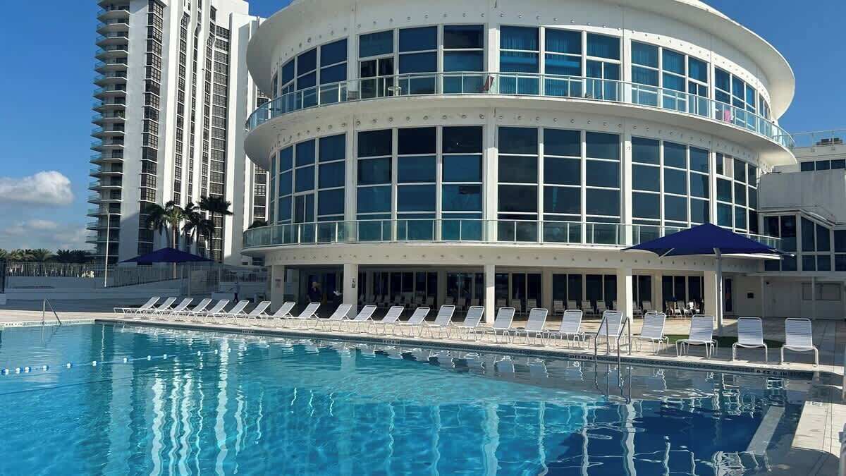 A hotel with a pool, lounge chairs, and a modern building with large windows.