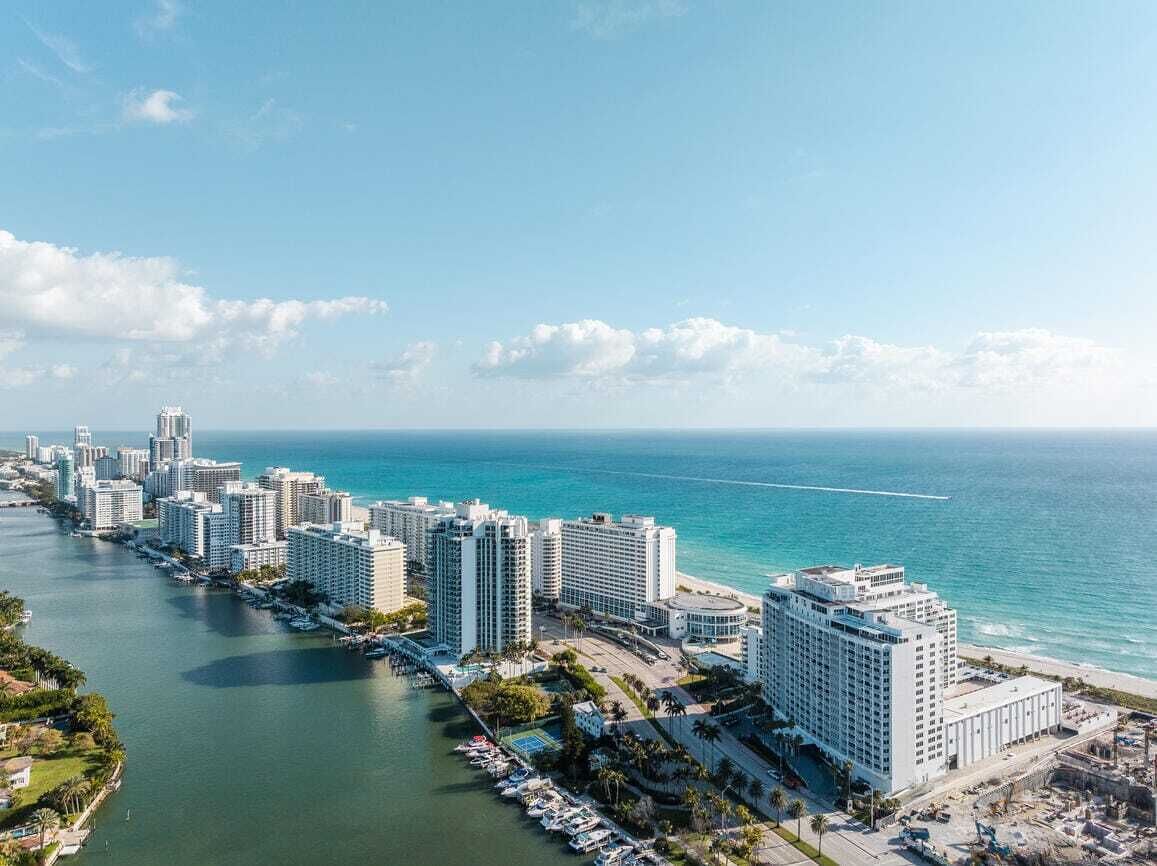 A coastal cityscape with high-rise hotels along the waterfront, a marina, and a clear view of the ocean.