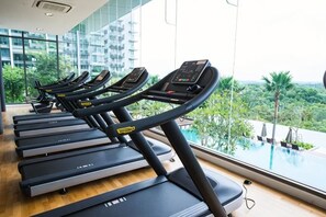 A row of treadmills in a gym with a view of a swimming pool and palm trees.