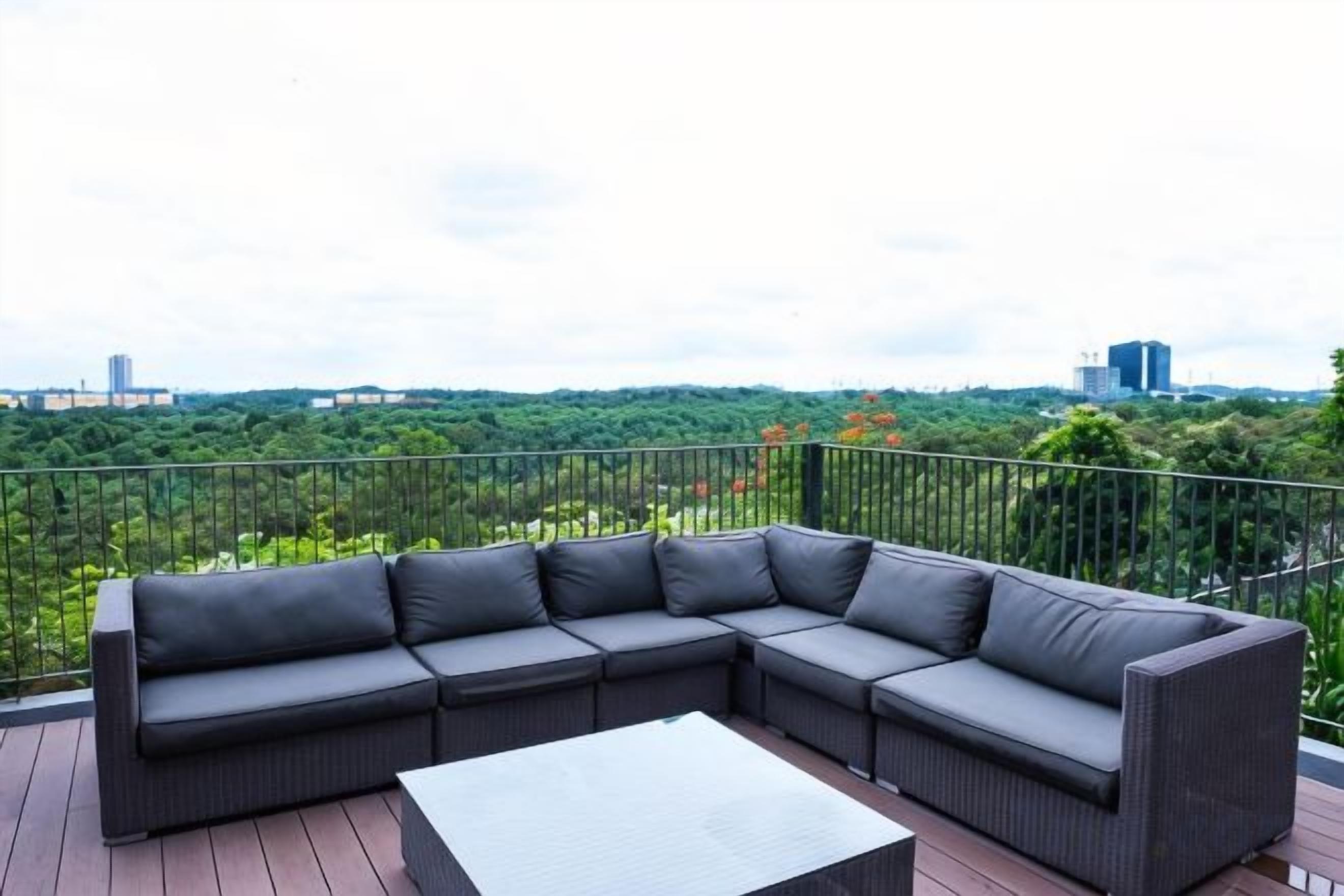 Un sofá modular en una terraza al aire libre con vistas a un paisaje urbano y vegetación.