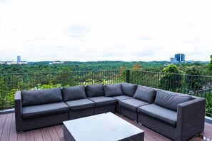 Un sofá modular en una terraza al aire libre con vistas a un paisaje urbano y vegetación.