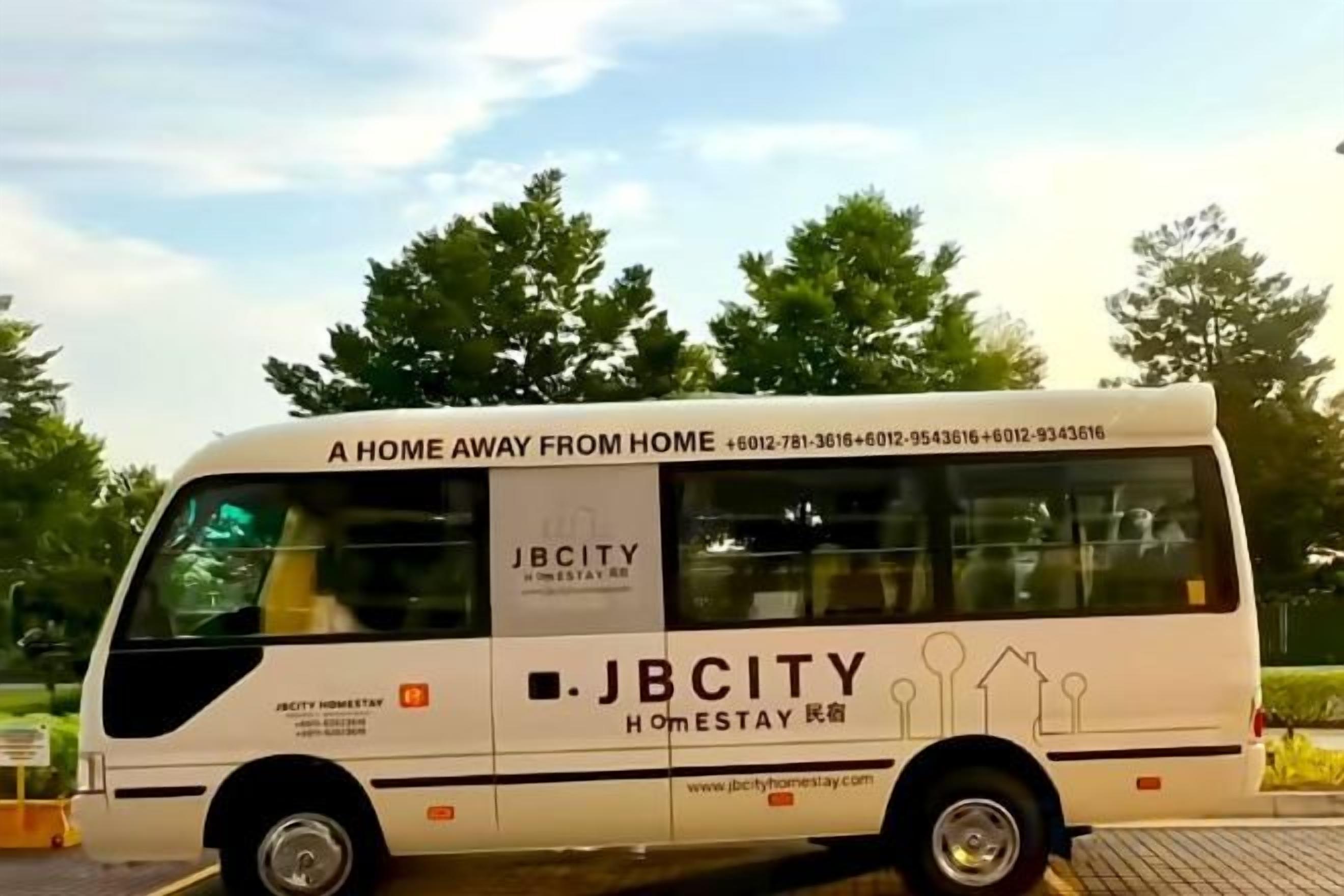 A white bus with 'JBCITY Homestay' branding and contact information.