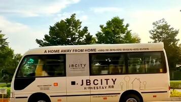 A white bus with 'JBCITY Homestay' branding and contact information.