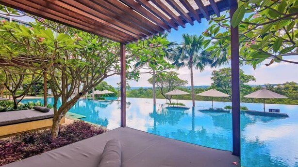 A poolside area with a lounge chair, umbrellas, and a view of the pool and surrounding greenery.