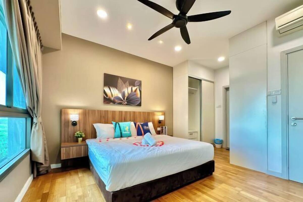 A modern bedroom with a large bed, a ceiling fan, a nightstand with a lamp, and a wall-mounted artwork.
