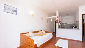 Ein Schlafzimmer mit einem hölzernen Bett, einem kleinen Tisch und einer Küche im Hintergrund.