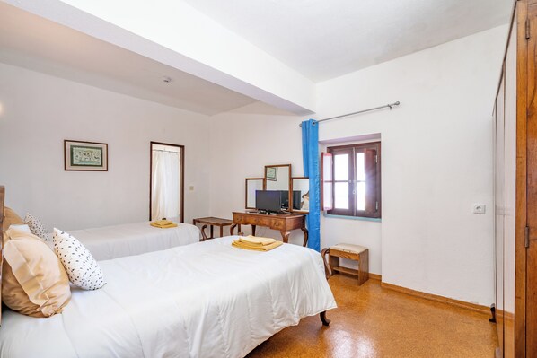 Una habitación con dos camas, un escritorio con computadora, una ventana con cortinas y una puerta.