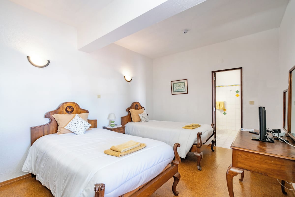 Una habitación de hotel con dos camas de madera, un escritorio y una silla. Hay luces fijadas a la pared y un cuadro enmarcado.