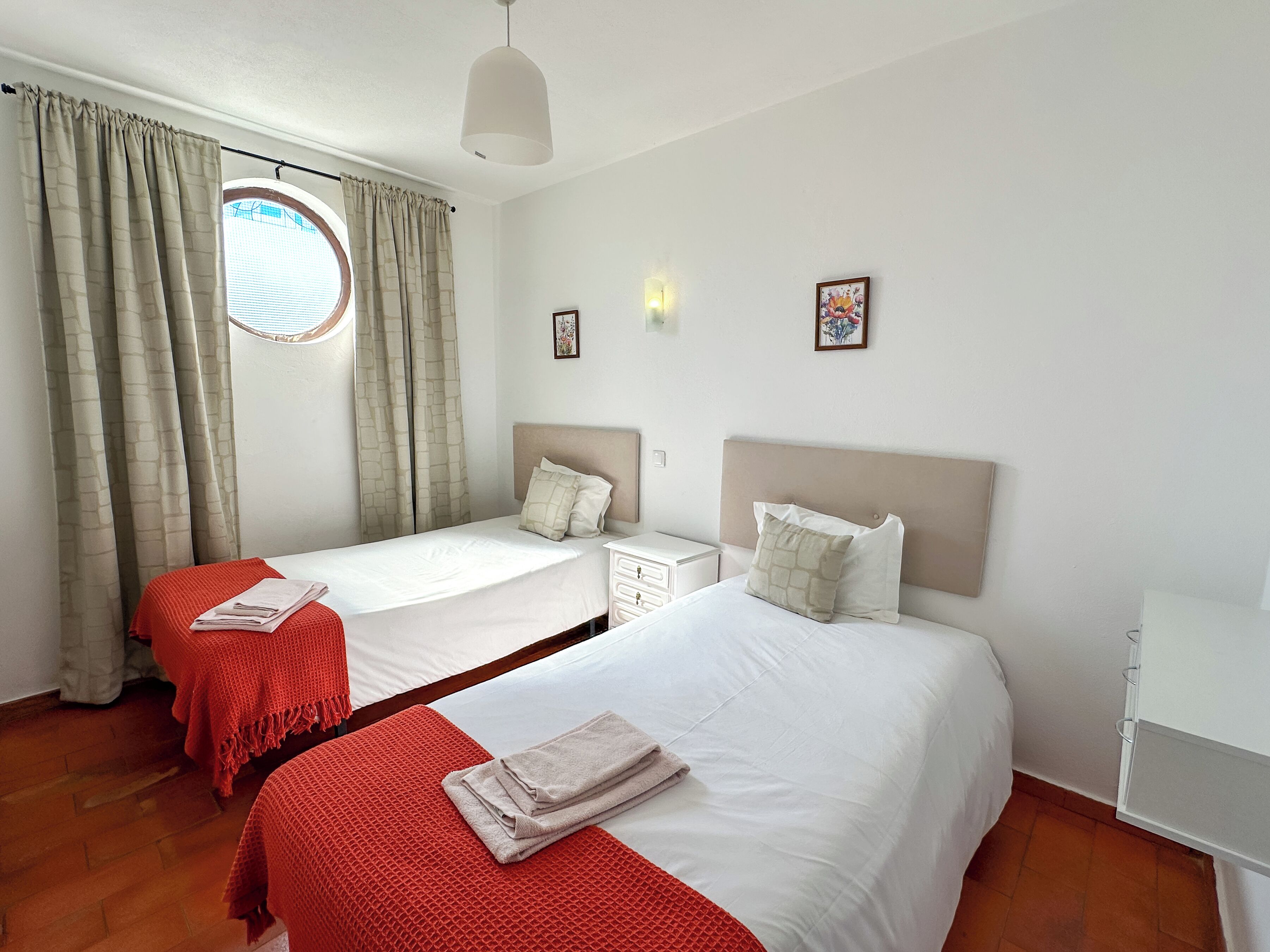 Une chambre d’hôtel avec deux lits, une fenêtre avec des rideaux, une petite table de chevet et une lampe fixée au mur.