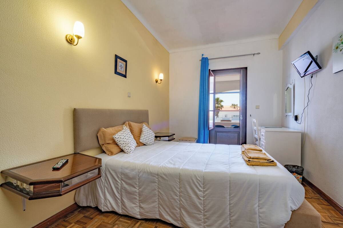 Habitación de hotel con cama, mesita de noche, televisor montado en la pared y vistas al exterior.