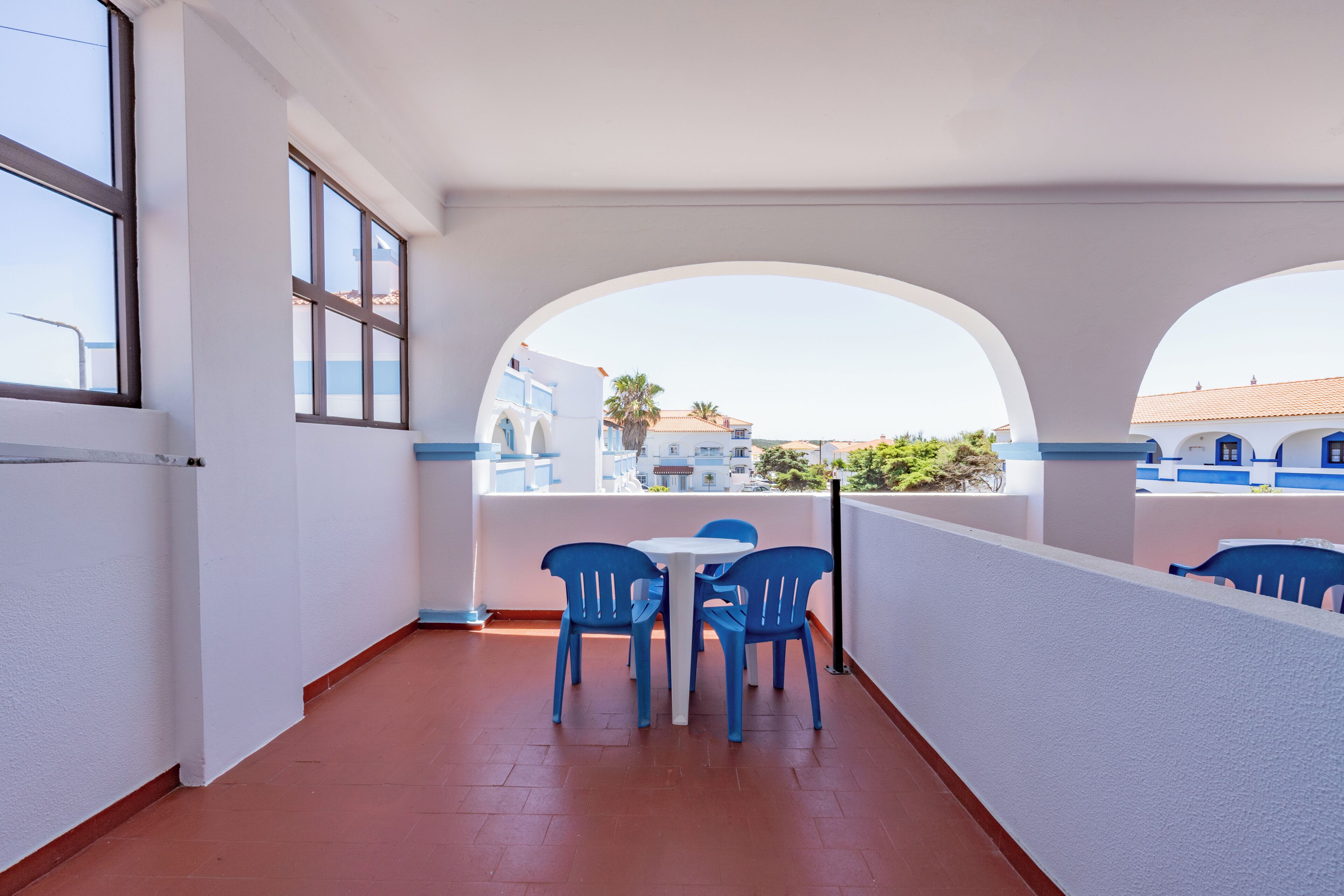 Un balcon avec une table blanche et des chaises bleues, donnant sur un quartier résidentiel avec des bâtiments bleus et blancs.