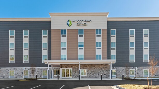 Un hôtel à l’architecture moderne, dont la façade présente en évidence un logo et l’inscription « Woodspring Suites ».