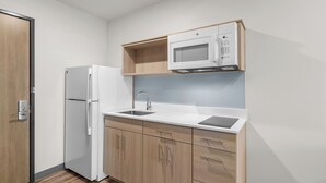 Une cuisine compacte équipée d’un four à micro-ondes encastré, d’un réfrigérateur et de meubles de rangement en bois.