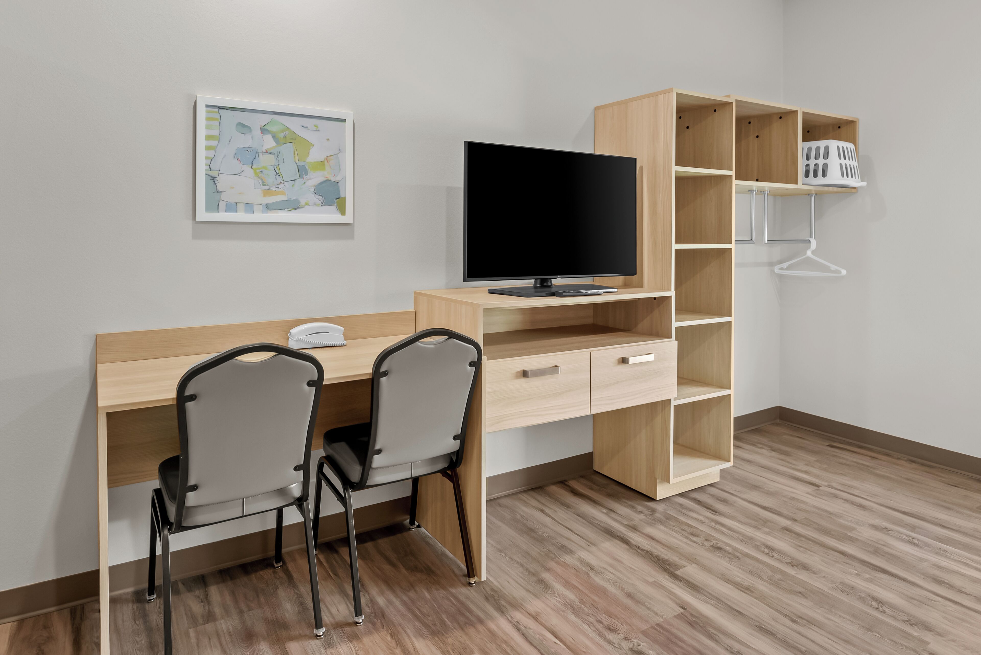 A modern room with a wooden desk, two chairs, a flat-screen TV, a map on the wall, and a wooden shelving unit.