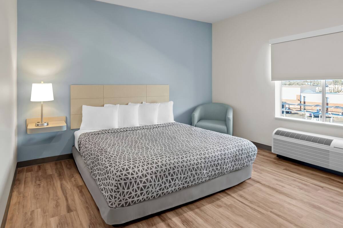 Een hotelkamer met een bed, een nachtkastje met lamp, een stoel en een raam met uitzicht.