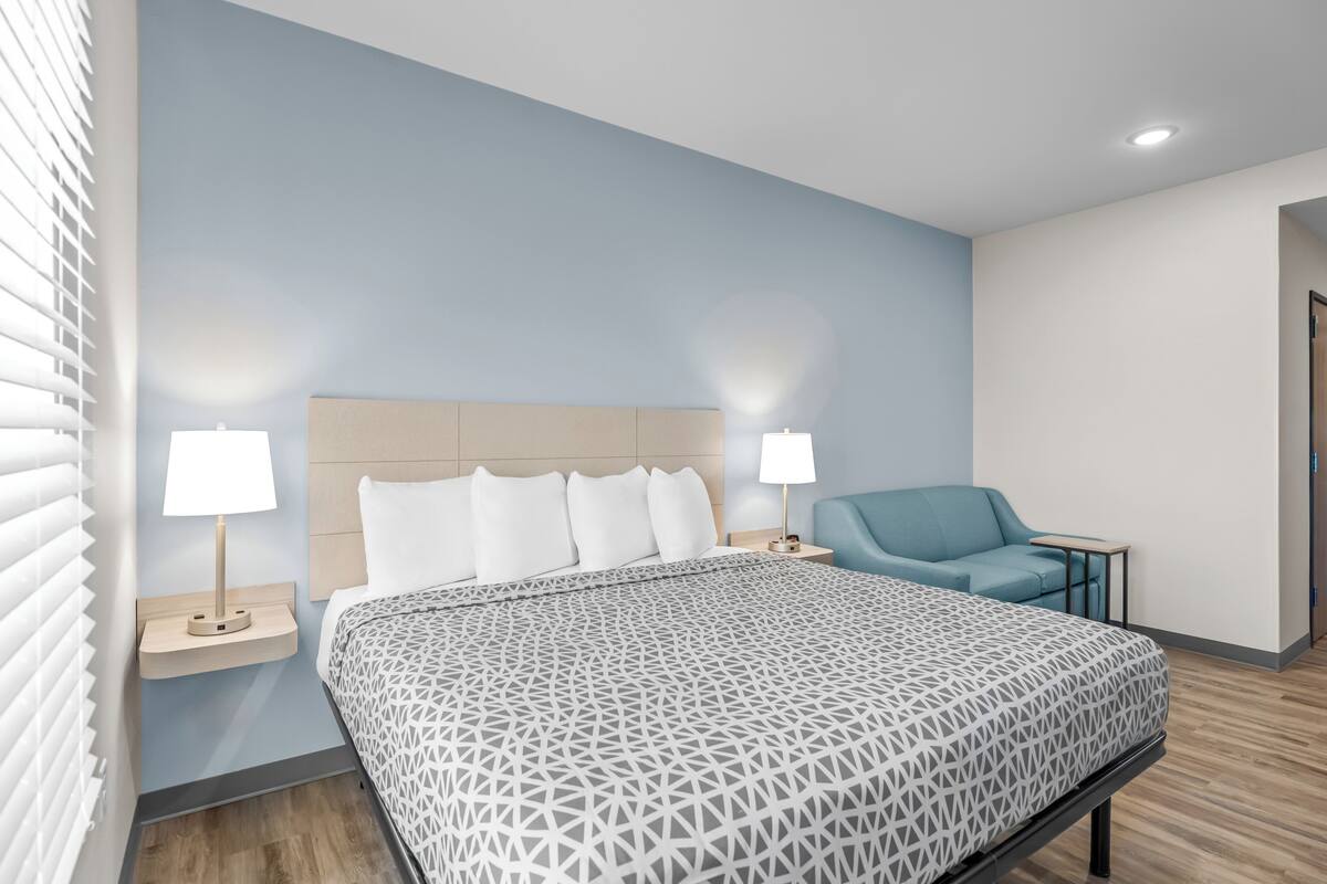 Een moderne hotelkamer met een groot bed, twee bedlampen, een blauwe fauteuil en een tafeltje.