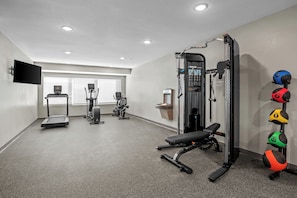 Une salle de sport équipée de tapis de course, d’une machine de musculation et de ballons d’exercice.