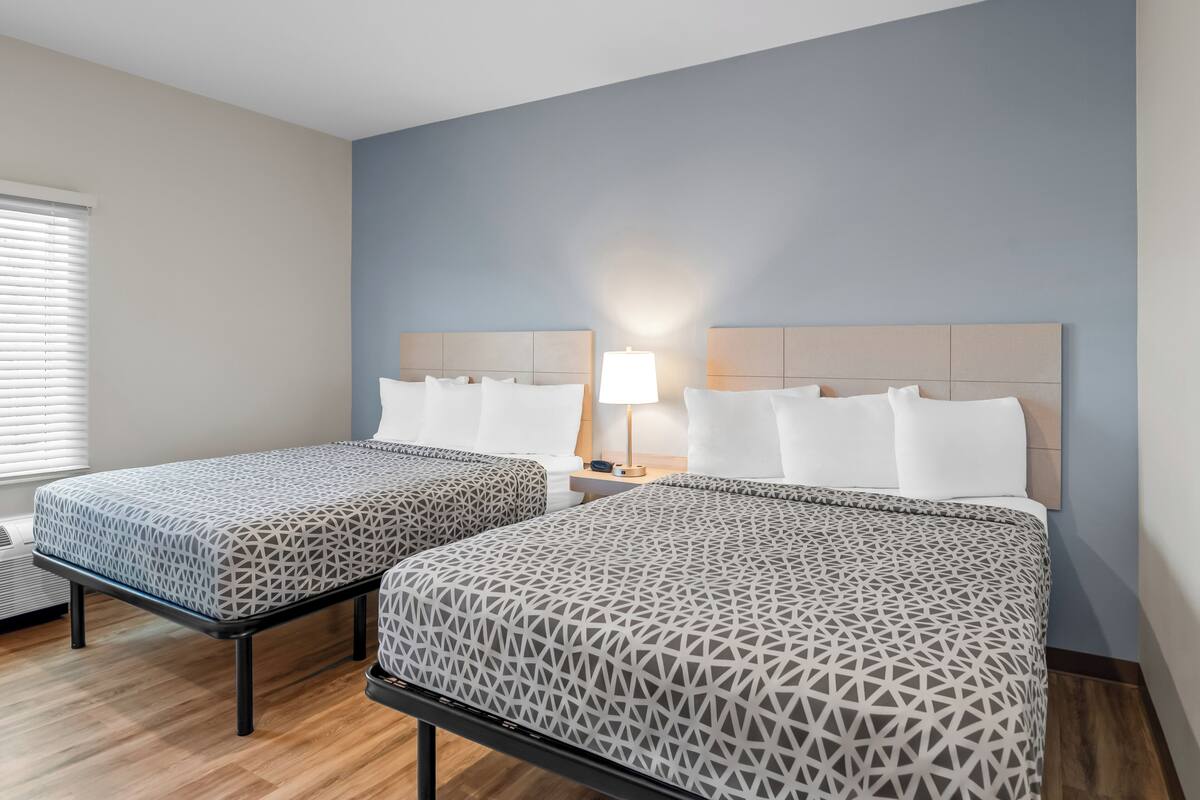Een hotelkamer met twee bedden, een nachtkastje met een lamp en een raam met jaloezieën.