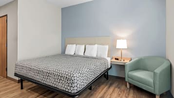 Una cama bien hecha con una colcha estampada, una lámpara de noche y un sillón verde en una habitación con suelo de madera y paredes azul claro.