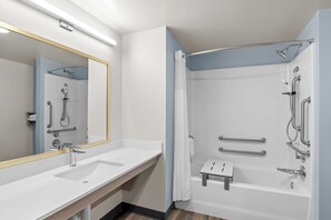 Une salle de bain moderne avec un grand miroir, deux lavabos, une douche équipée de barres d’appui et un petit tabouret.