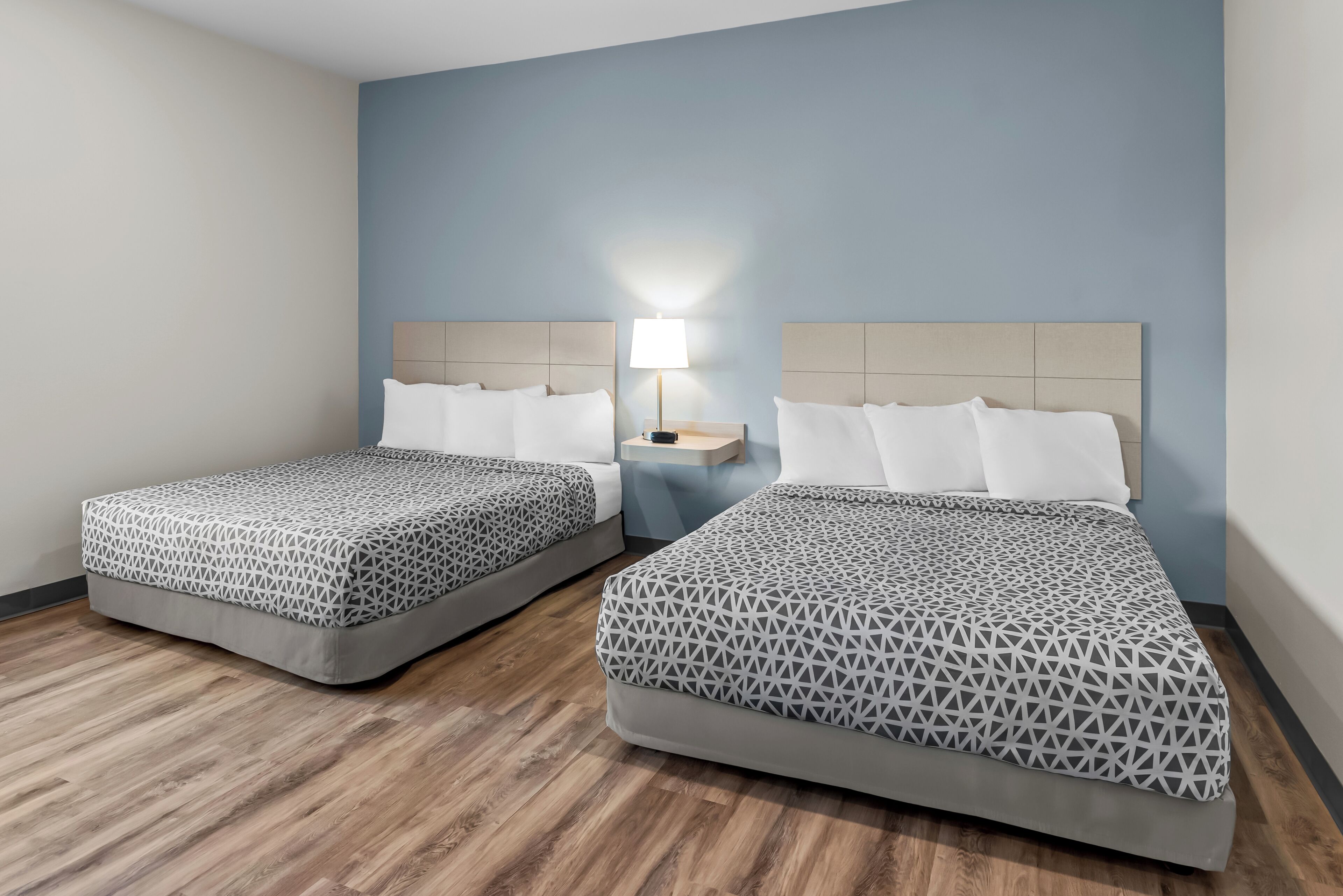 Two single beds with patterned bedding, a nightstand with a lamp, and wooden flooring.