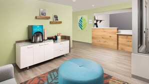 A modern hotel room with a kitchenette, a blue ottoman, and a colorful rug. - WoodSpring Suites Cleveland North (Cleveland)