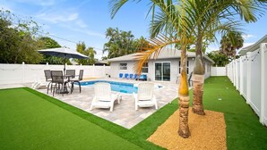 A backyard with a swimming pool, patio furniture, and palm trees. - The Club at Naples Park | Pool, Bocce & Putting Green (Naples)