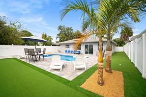 A backyard with a swimming pool, patio furniture, and palm trees. - The Club at Naples Park | Pool, Bocce & Putting Green (Naples)