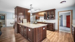 A spacious kitchen with dark wooden cabinets, a large island, and a modern light fixture. - The Club at Naples Park | Pool, Bocce & Putting Green (Naples)