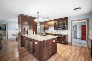 A spacious kitchen with dark wooden cabinets, a large island, and a modern light fixture. - The Club at Naples Park | Pool, Bocce & Putting Green (Naples)