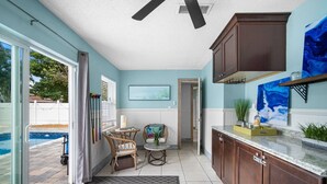 A kitchen with a pool view, a dining area with chairs, and a ceiling fan. - The Club at Naples Park | Pool, Bocce & Putting Green (Naples)