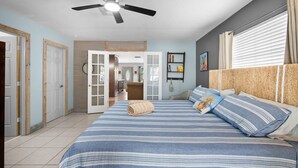 A bedroom with a bed, a ceiling fan, a window with curtains, and a door leading to another room. - The Club at Naples Park | Pool, Bocce & Putting Green (Naples)