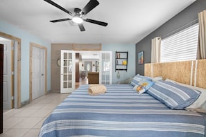 A bedroom with a bed, a ceiling fan, a window with curtains, and a door leading to another room. - The Club at Naples Park | Pool, Bocce & Putting Green (Naples)