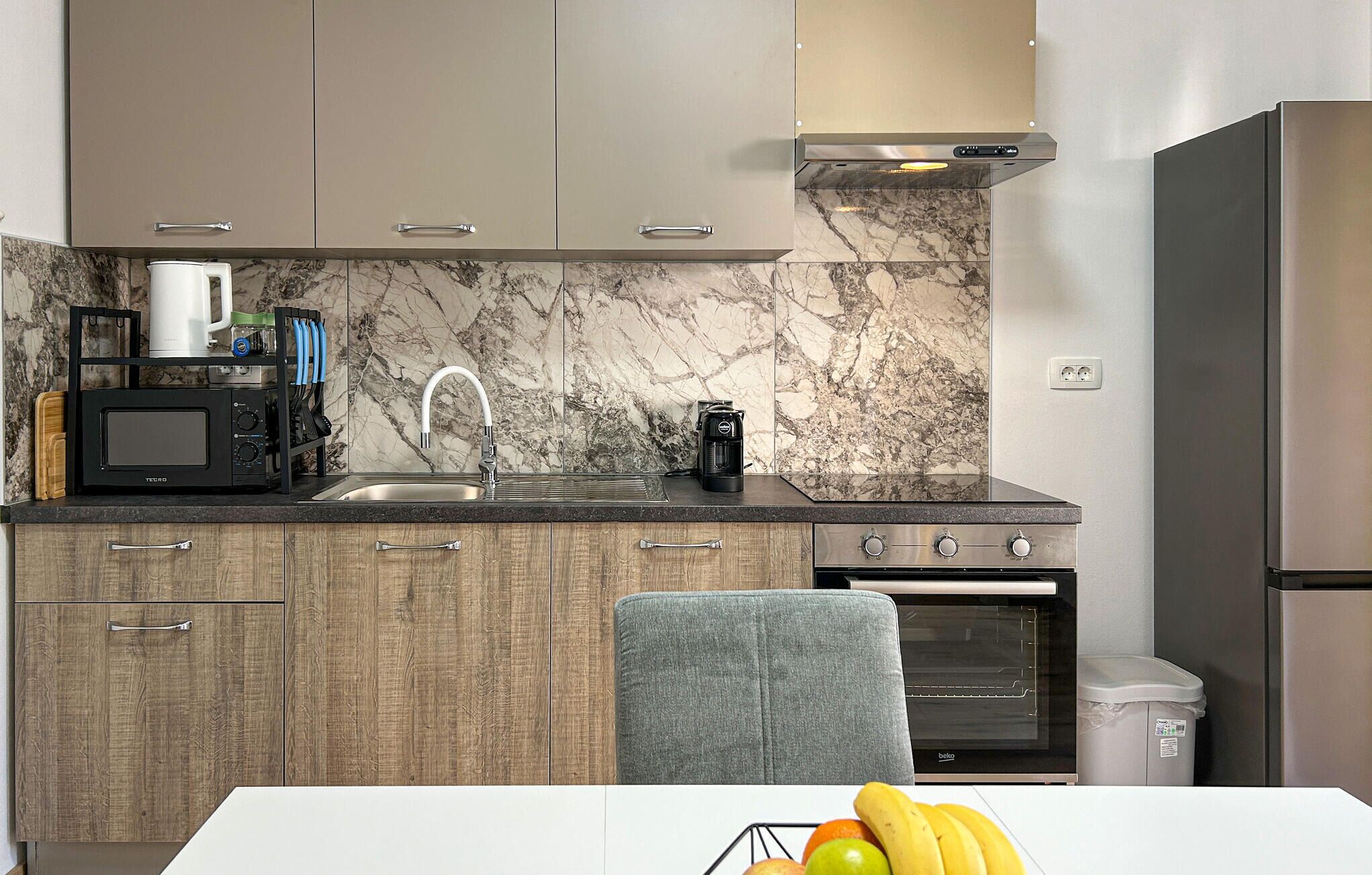 Uma cozinha moderna com painel de backsplash de mármore, forno embutido, cafeteira e micro-ondas.