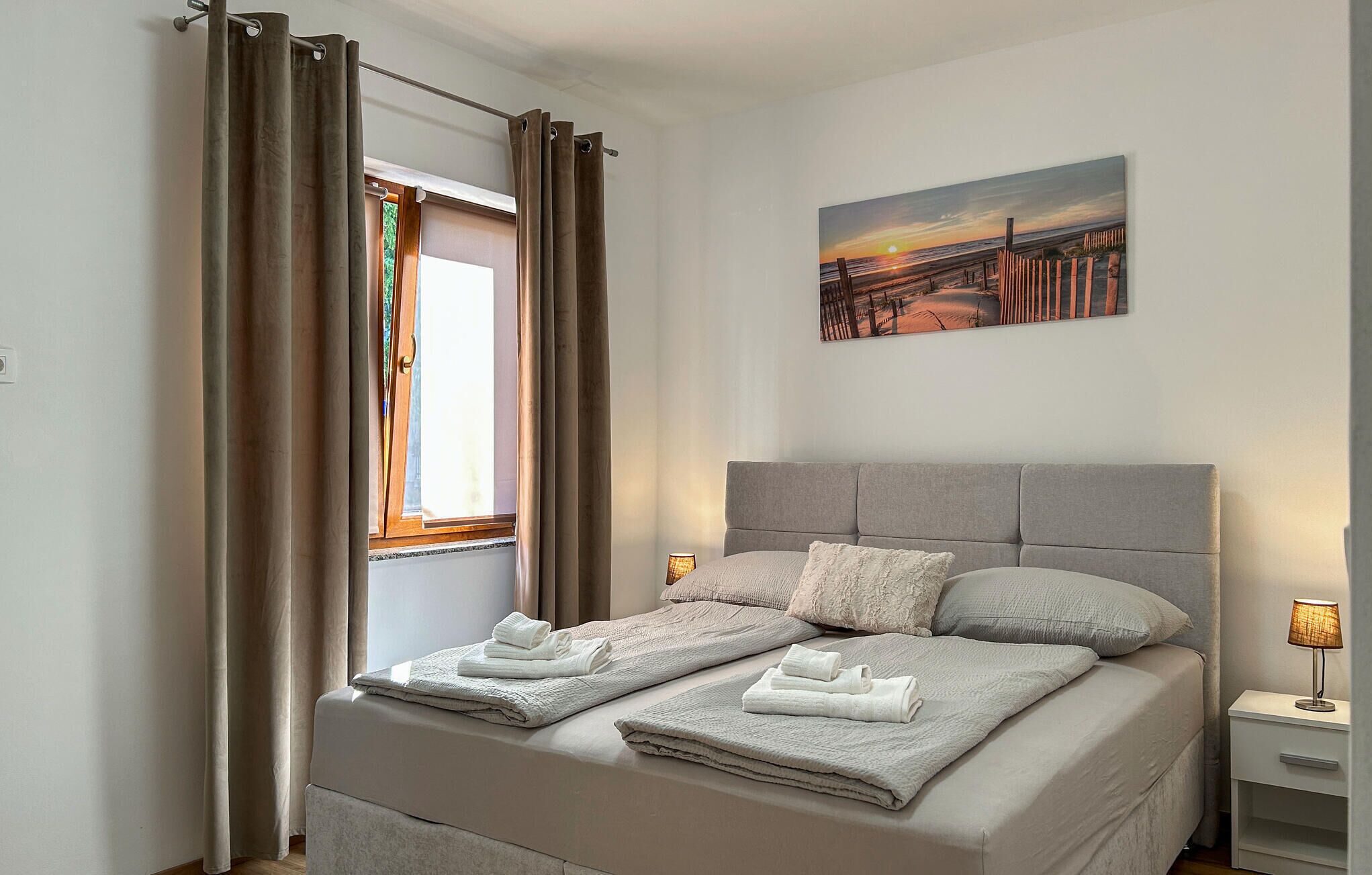 A bedroom with a bed, curtains, a painting, and a nightstand.