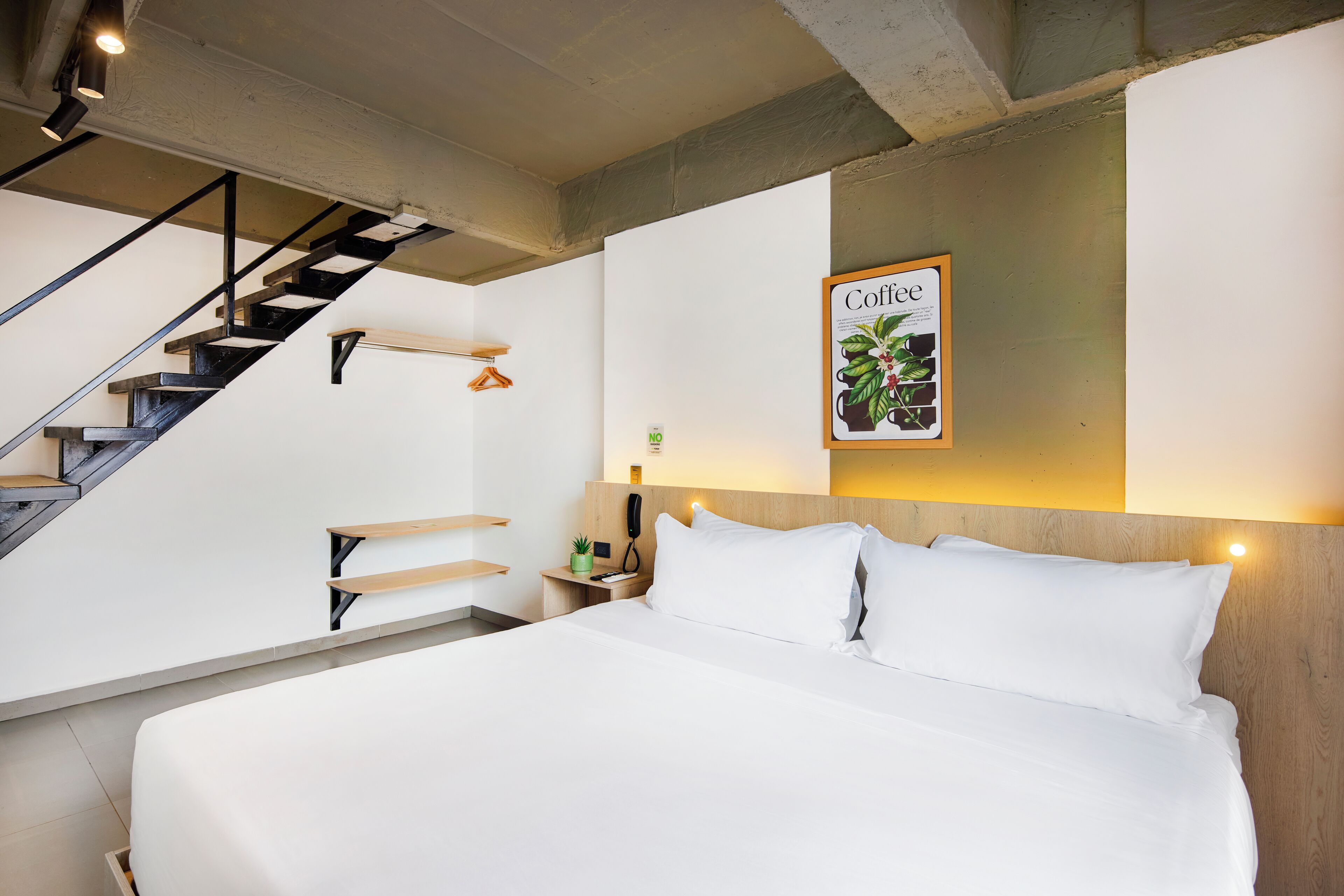A modern hotel room with a large bed, a wooden headboard, a staircase, and a wall-mounted artwork titled "Coffee".