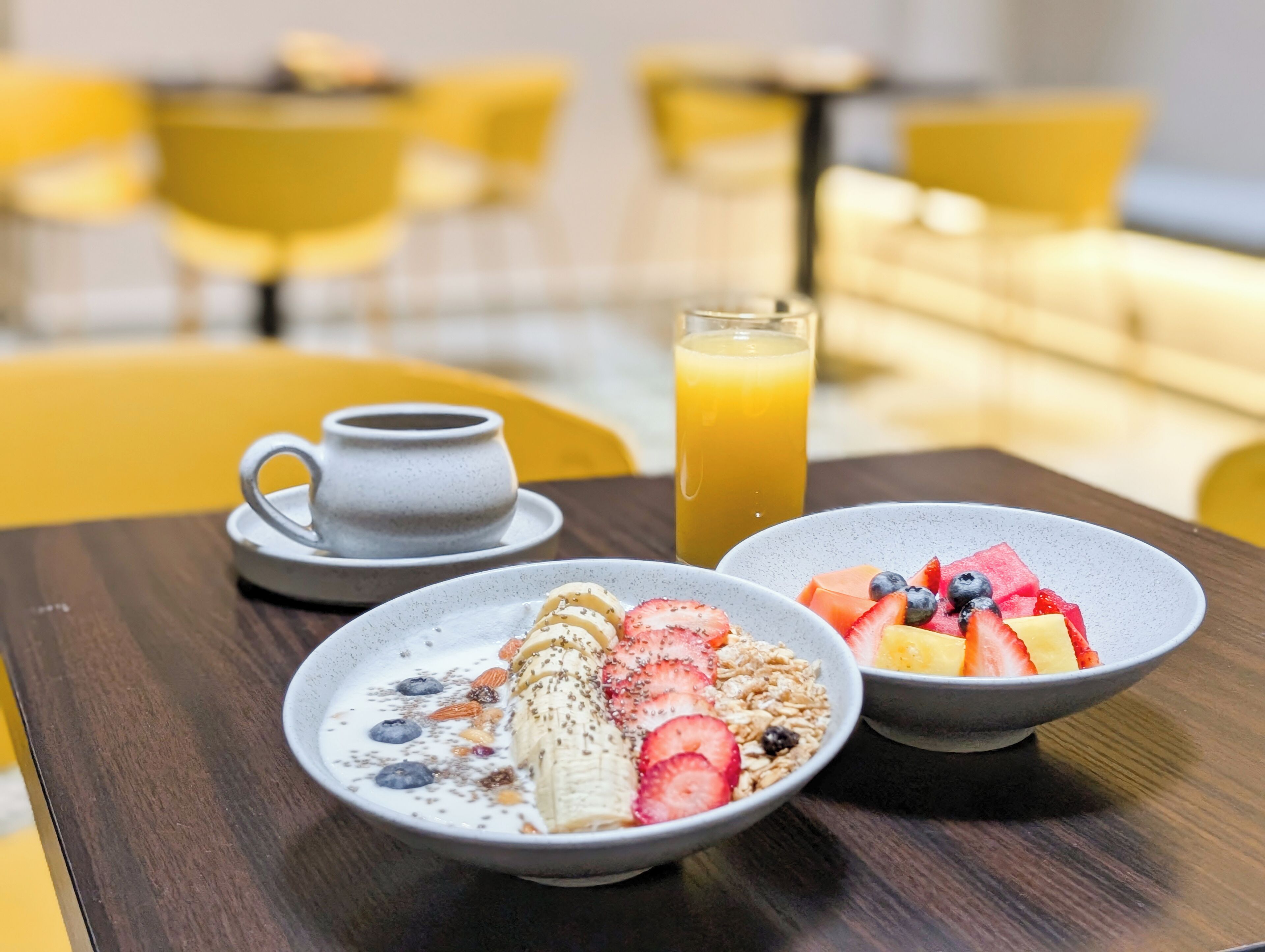 Desayuno con dos tazones de cereal cubiertos de frutas y un vaso de jugo de naranja sobre una mesa de madera.