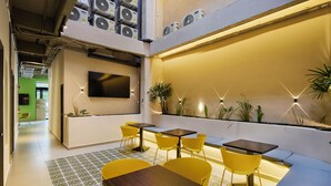A modern interior with yellow chairs and tables, a flat-screen TV mounted on the wall, and a large window overlooking a green outdoor area. - Hotel Attic 33 (Medellín)